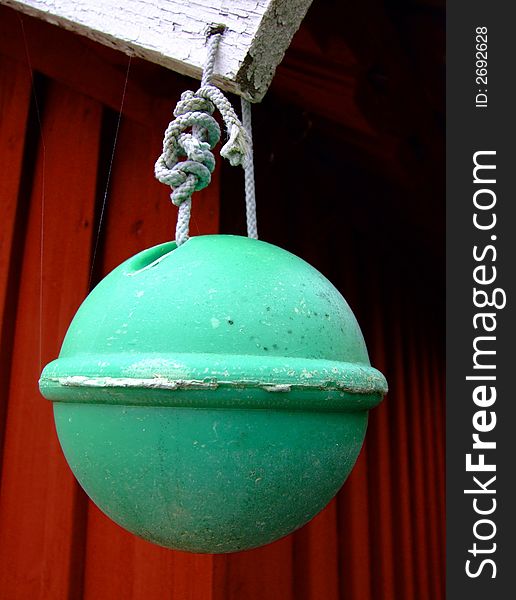 A green boatbuoy hanging from the roof of a red woodenhouse, Sweden.