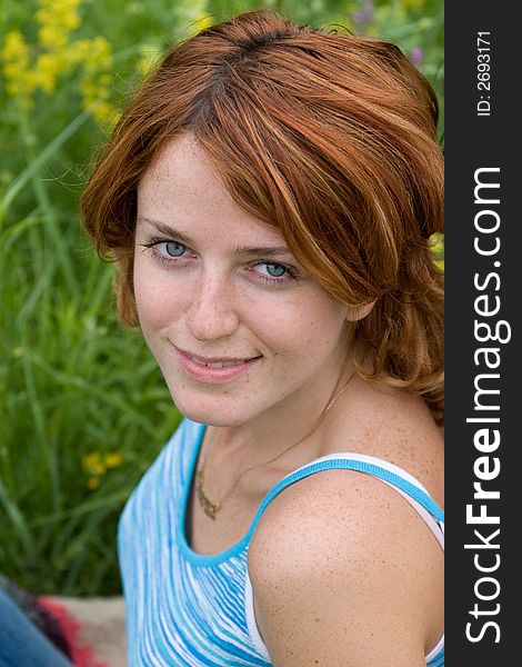 Outdoor shot of red-haired girl sitting on summer meadow and looking upward. Outdoor shot of red-haired girl sitting on summer meadow and looking upward