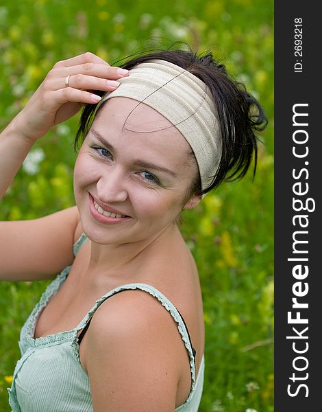 Outdoor shot of black-haired girl sitting on summer meadow and touching her head. Outdoor shot of black-haired girl sitting on summer meadow and touching her head