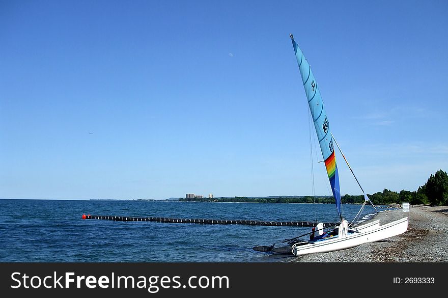 A beached sailboat next to the water with dock, the coastline, horizon and blue sky in the background.