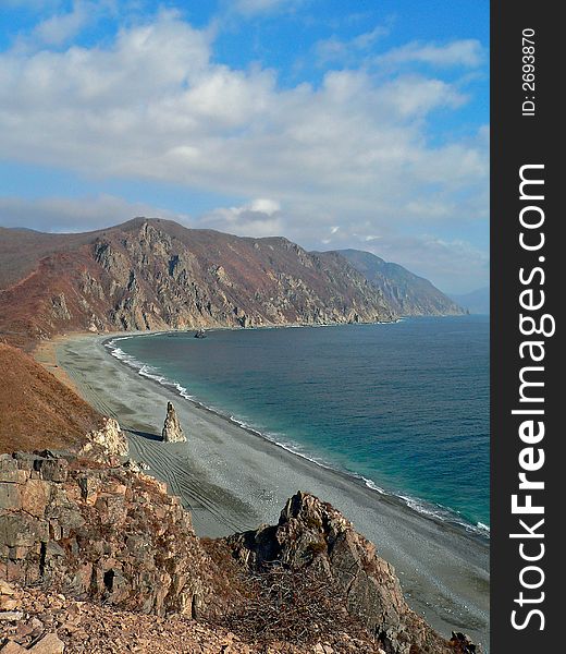 A cloudscape on sea: turquoise sea, grey beach, yellow-red capes and white clouds on azure sky. Autumn. Pastel. Vertical. Russian Far East, Primorye, Japanese sea, Tasovaya bay. A cloudscape on sea: turquoise sea, grey beach, yellow-red capes and white clouds on azure sky. Autumn. Pastel. Vertical. Russian Far East, Primorye, Japanese sea, Tasovaya bay.