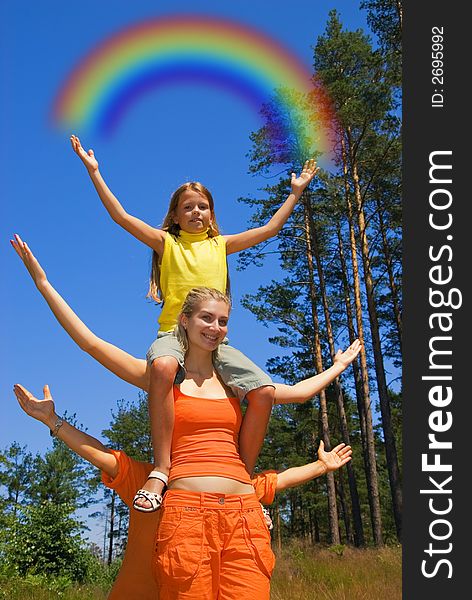 Small girl sitting on a sister's shoulders  holding  rainbow in her hands. Small girl sitting on a sister's shoulders  holding  rainbow in her hands