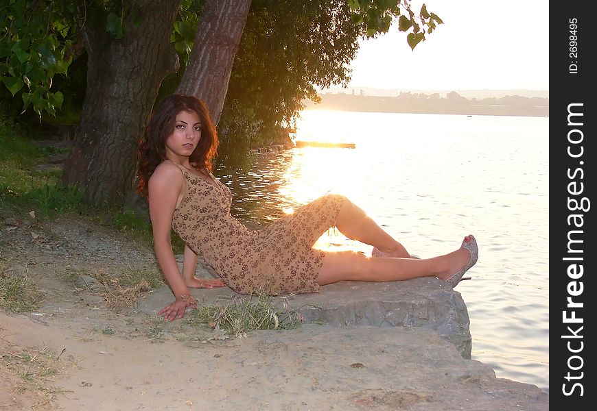 An lovely young lady sitting on a big rock on the lake relaxing by sunset. An lovely young lady sitting on a big rock on the lake relaxing by sunset.