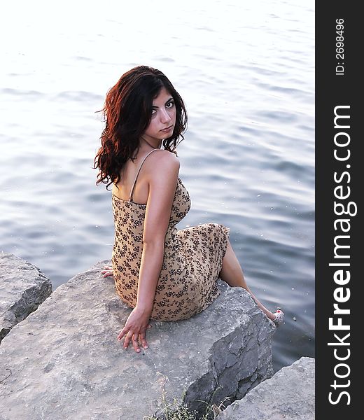 An lovely young lady sitting on a big rock on the lake relaxing by sunset. An lovely young lady sitting on a big rock on the lake relaxing by sunset.