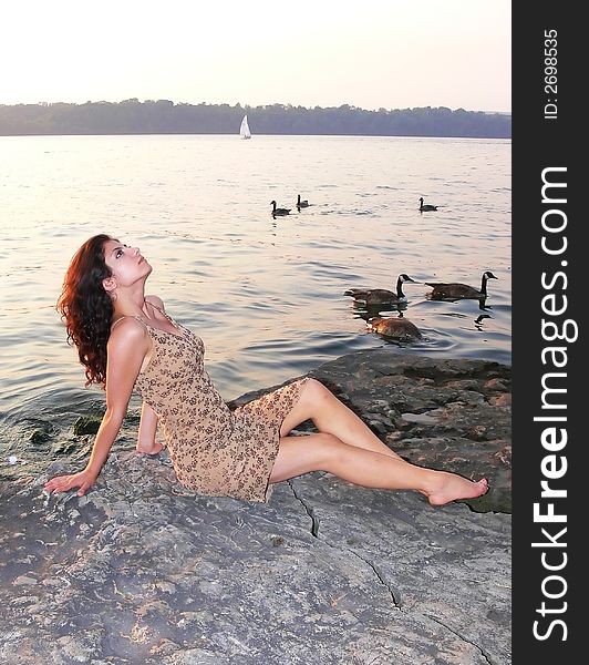 An lovely young lady sitting on a big rock on the lake relaxing by sunset. An lovely young lady sitting on a big rock on the lake relaxing by sunset.