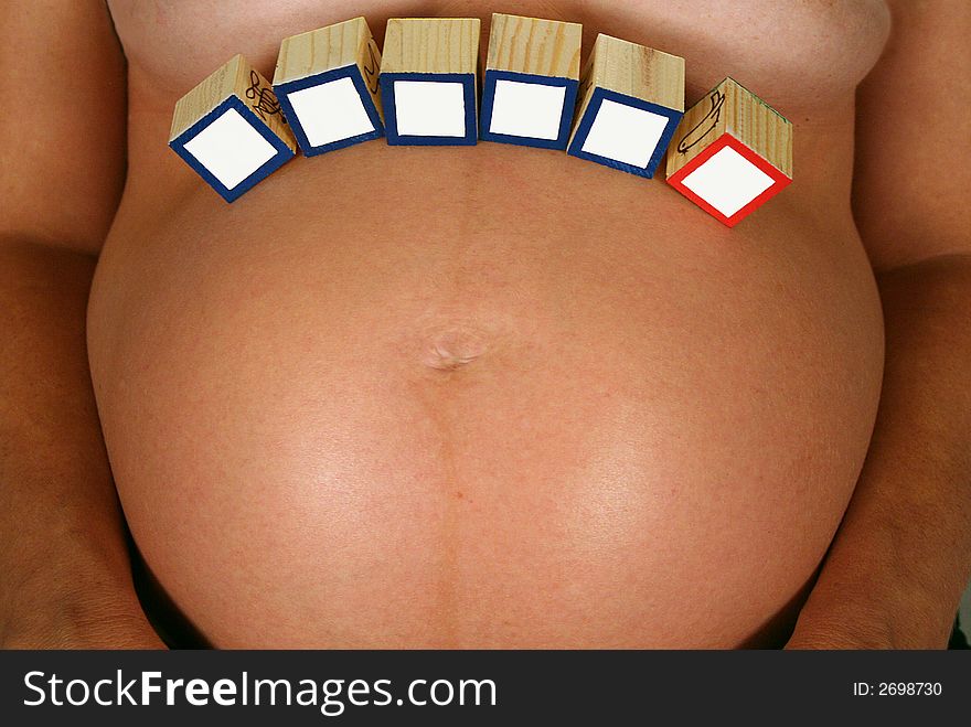 Some blank baby blocks are balanced on a woman't pregnant stomach. Some blank baby blocks are balanced on a woman't pregnant stomach.