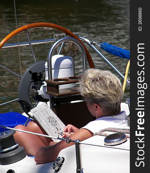 Woman sitting on a sailboat doing a crossword puzzle. Woman sitting on a sailboat doing a crossword puzzle