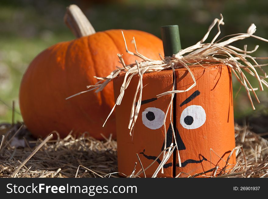 A crafty creation of a wooden pumpkin head replica sets atop a hay bale. A crafty creation of a wooden pumpkin head replica sets atop a hay bale.