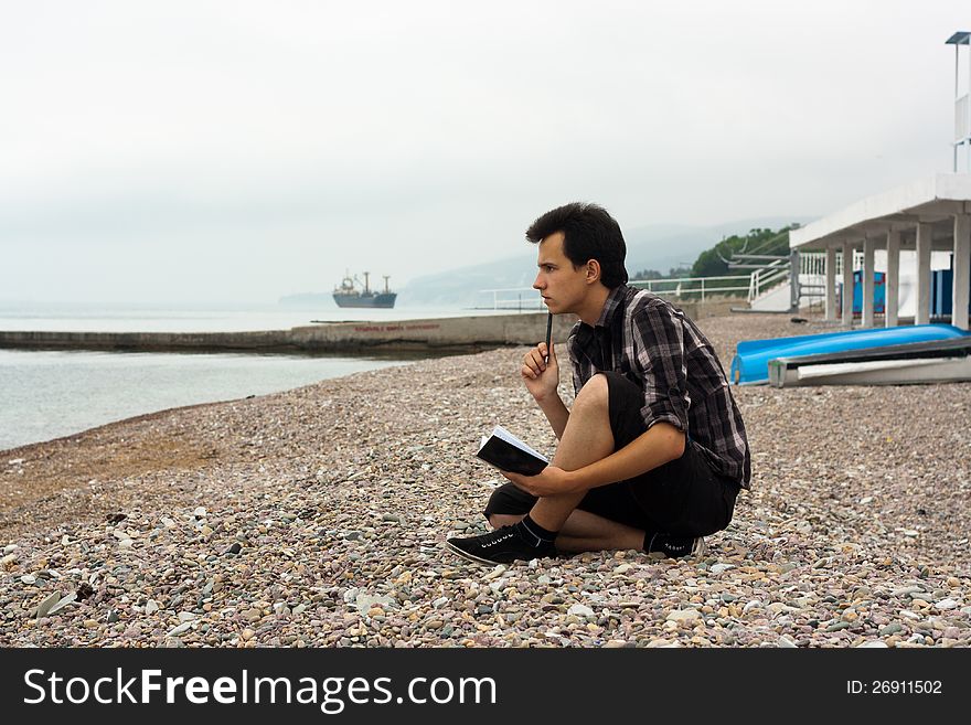 Boy sit on the sea stones and write in notebook. Boy sit on the sea stones and write in notebook