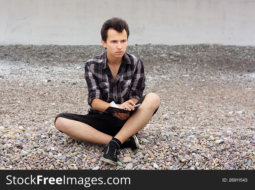 Boy sit on the sea stones and write in notebook. Boy sit on the sea stones and write in notebook