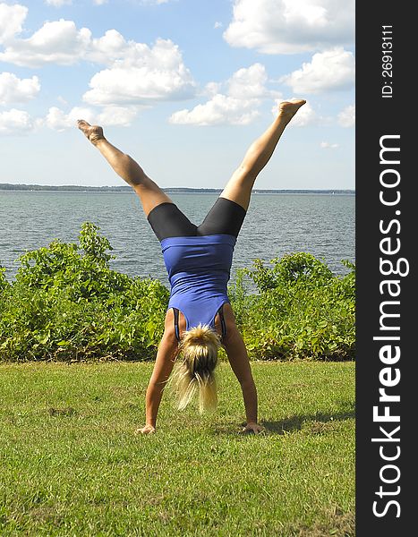An athletic girl does a hand stand on the lawn by a lake. An athletic girl does a hand stand on the lawn by a lake.