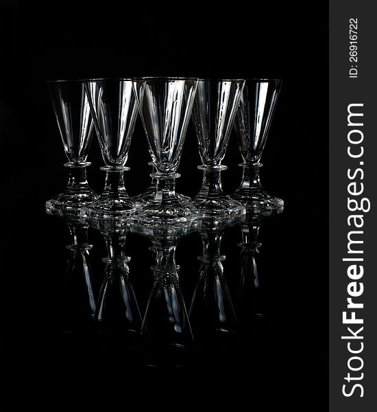 The six old crystal shot glasses on a glass plate with a black background