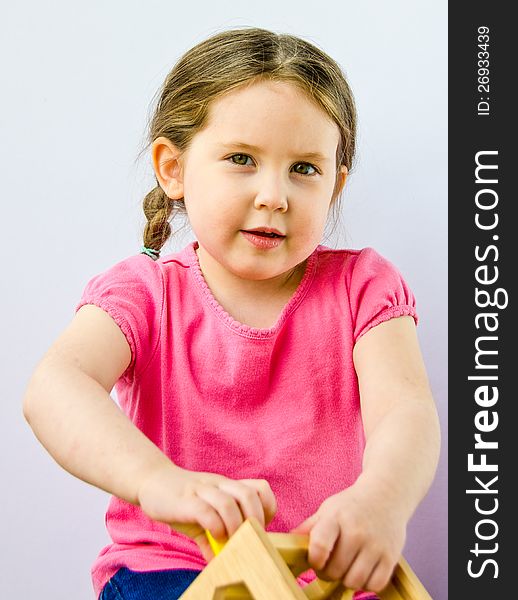 Close up of pretty three-year-old girl with braids plays with block puzzle isolated on white. Close up of pretty three-year-old girl with braids plays with block puzzle isolated on white.