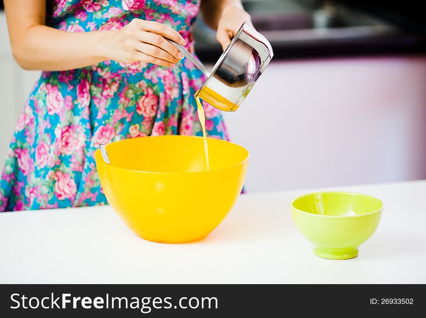 Pouring out melted butter from a metallic pot to an orange plastic bowl at homely kitchen. Pouring out melted butter from a metallic pot to an orange plastic bowl at homely kitchen