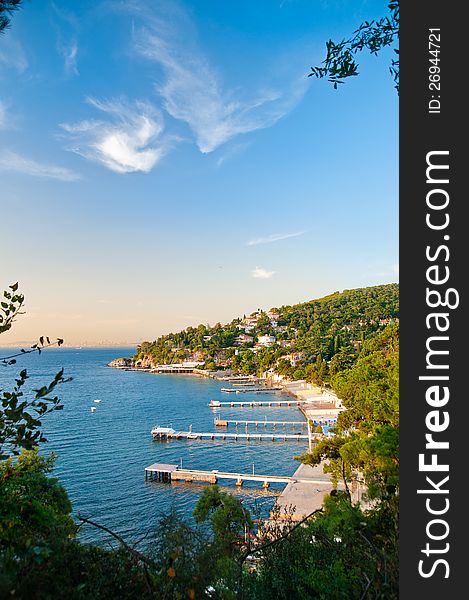 Vertical photo of a beach with many piers. Sky and sea is perfectly blue, the beach is near the mountains, full of trees. Vertical photo of a beach with many piers. Sky and sea is perfectly blue, the beach is near the mountains, full of trees.