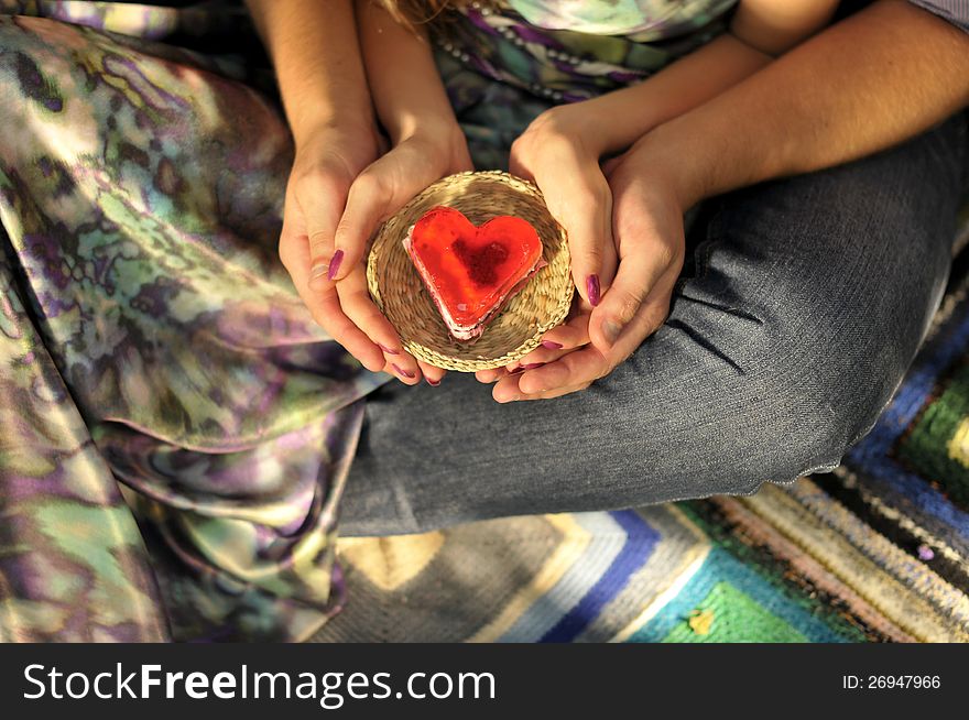 Cake in the shape of a heart on a straw saucer in hands. Cake in the shape of a heart on a straw saucer in hands