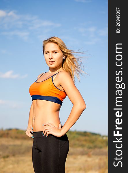Beautiful blonde woman with a shapely body posing with a bare midriff in open countryside with the wind in her hair. Beautiful blonde woman with a shapely body posing with a bare midriff in open countryside with the wind in her hair