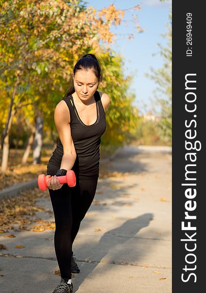 Fit muscular woman working out with weights flexing her arm and raising a dumbbell standing on a rural road