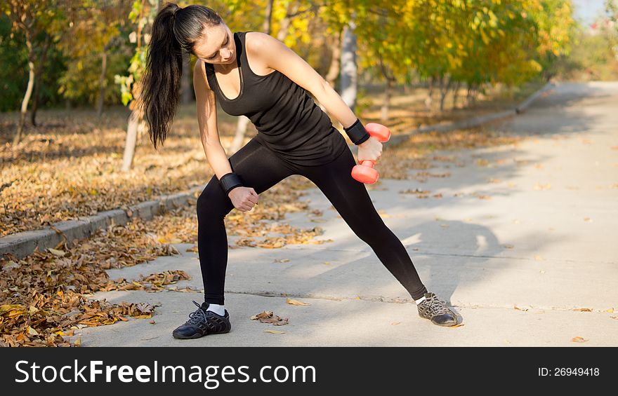 Woman in sportswear leaning forward and raising her arm to the side while working out with a dumbbell. Woman in sportswear leaning forward and raising her arm to the side while working out with a dumbbell