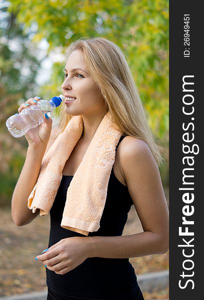 Attractive blonde female athlete drinking bottled water for hydration after working out in the park doing exercises