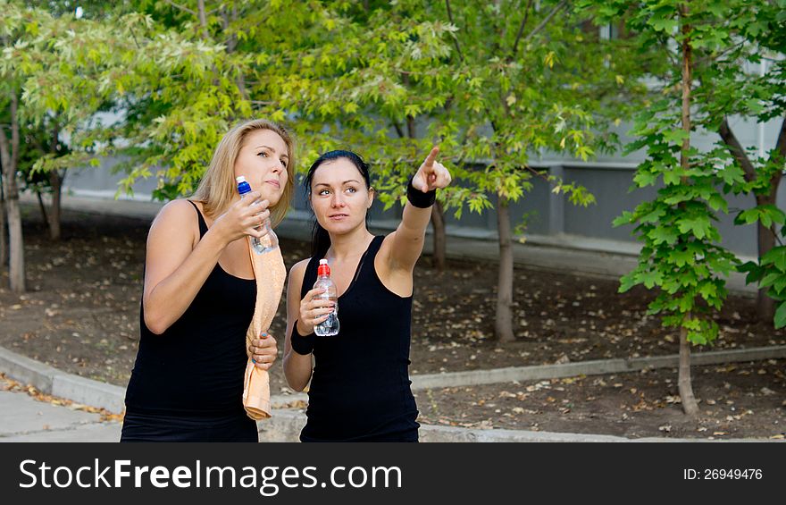 Woman athlete pointing her hand and showing something to her teammate as they stop during training for a drink of water