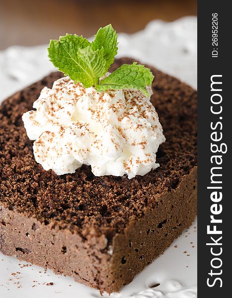 Piece of chocolate cake with whipped cream and mint on a white plate