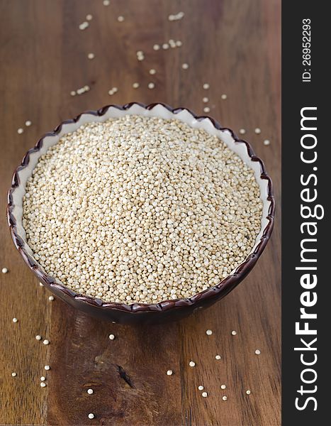 Dry grain quinoa in a ceramic bowl on wooden table