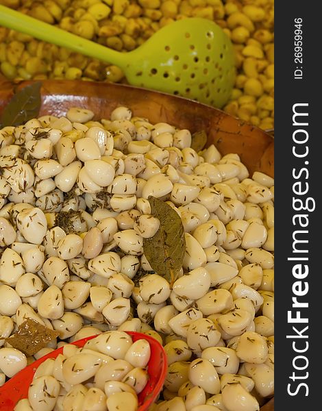 Pickled garlic with spices and herbs at the market. Olives in the background.