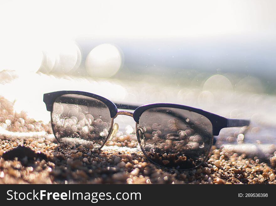 Sunglasses on a sandy beach. Sunset by the sea. Background in bokeh. Vacation at the sea. Flight to the journey.