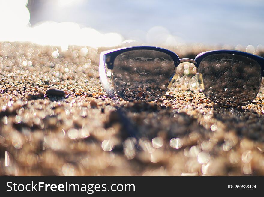 Sunglasses On A Sandy Beach. Sunset By The Sea. Background In Bokeh. Vacation At The Sea. Flight To The Journey.