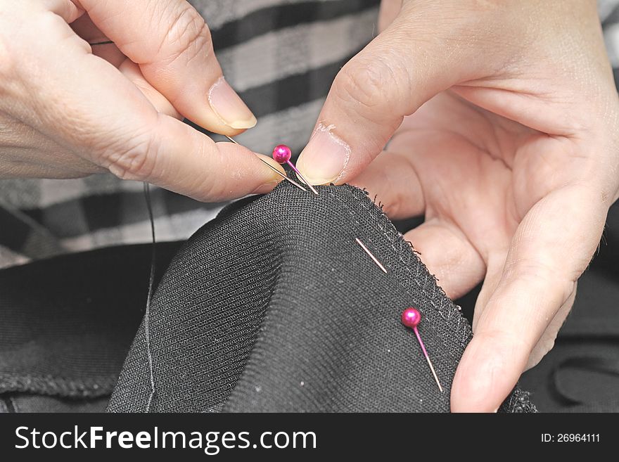 Female hands is sewing black dress. Female hands is sewing black dress