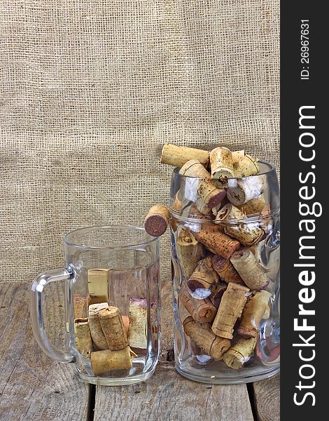 Two beer mugs filled with corks from wine bottles are on the rough wooden table. Sackcloth background. Two beer mugs filled with corks from wine bottles are on the rough wooden table. Sackcloth background