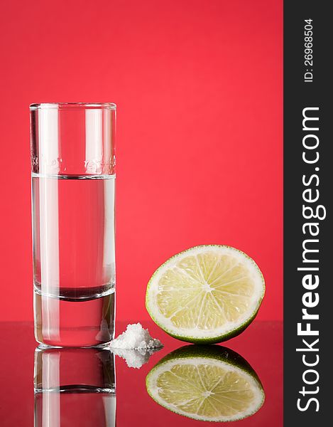Tequila in a glass with a slice of lemon on a red background