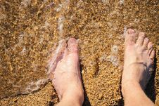 Men S Feet Are Standing On A Sandy Beach. Small Waves Are Foaming On The Seashore. Crystal Water. Royalty Free Stock Photography