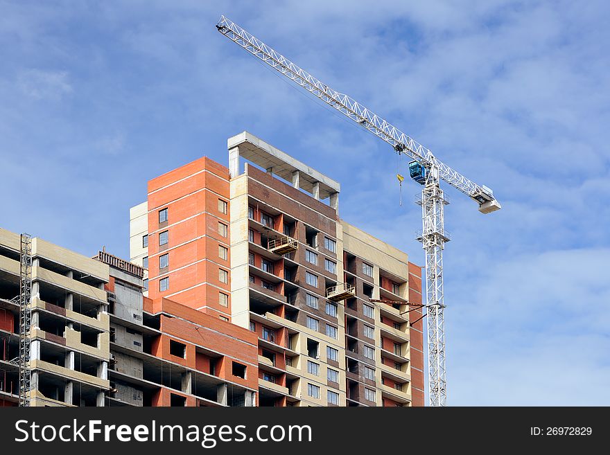 The crane and the house under construction against the sky. The crane and the house under construction against the sky