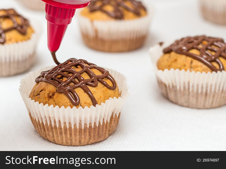 Muffins on a white paper towel getting a chocolate glaze with a decoration bag. Muffins on a white paper towel getting a chocolate glaze with a decoration bag.