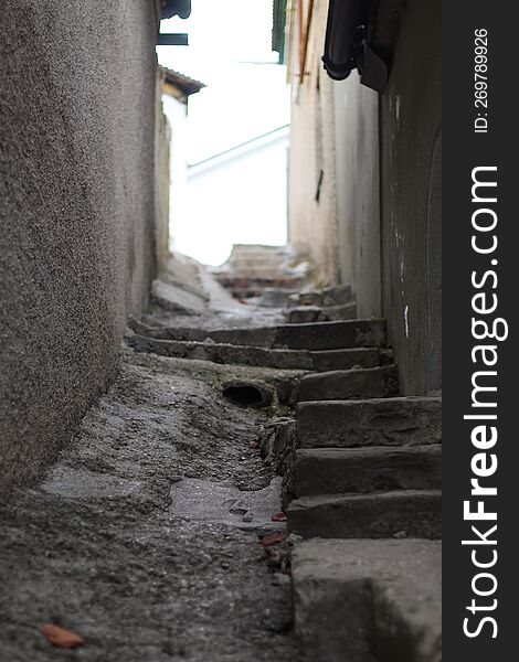 An Old Staircase In A Narrow Alley Between The Houses. Hilly Area Of The City. A Drain On The Street.