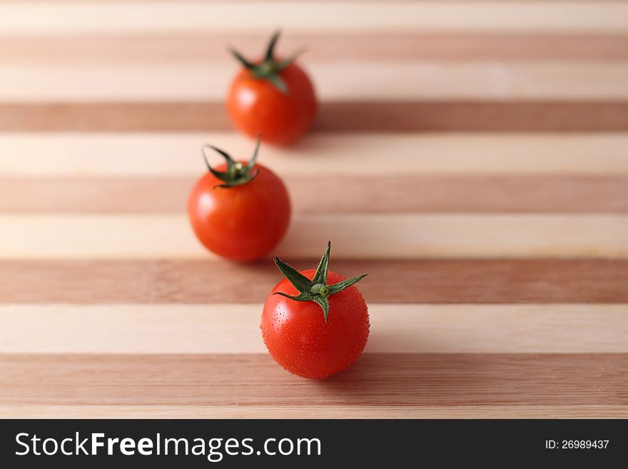 Three red cherry tomatoes with wooden chopping board .