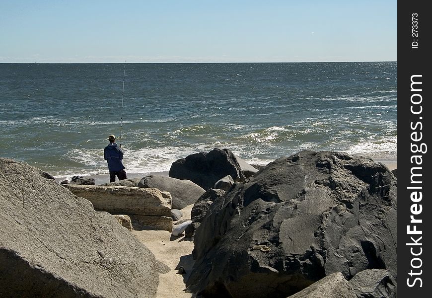 A man fishing along a rocky shoreline at Sandy Hook, NJ. A man fishing along a rocky shoreline at Sandy Hook, NJ.