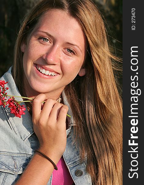 A beautiful teen-aged girl smiling and holding a flower. A beautiful teen-aged girl smiling and holding a flower.