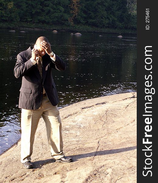 Business man standing by a river talking on cell phone looking upset. Shot in hard natural light. Business man standing by a river talking on cell phone looking upset. Shot in hard natural light.