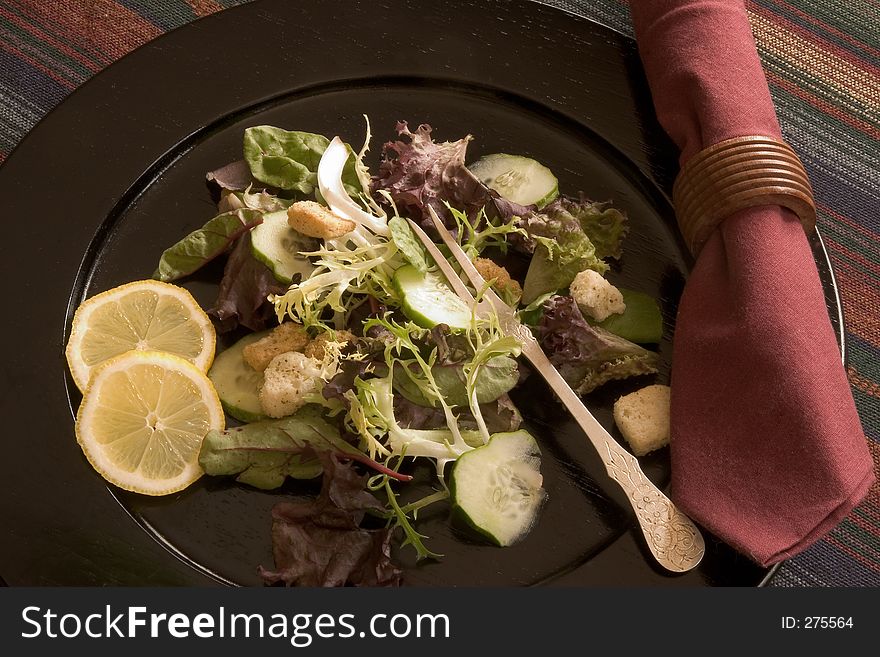 Salad on black plate with lemons and napkin. Salad on black plate with lemons and napkin