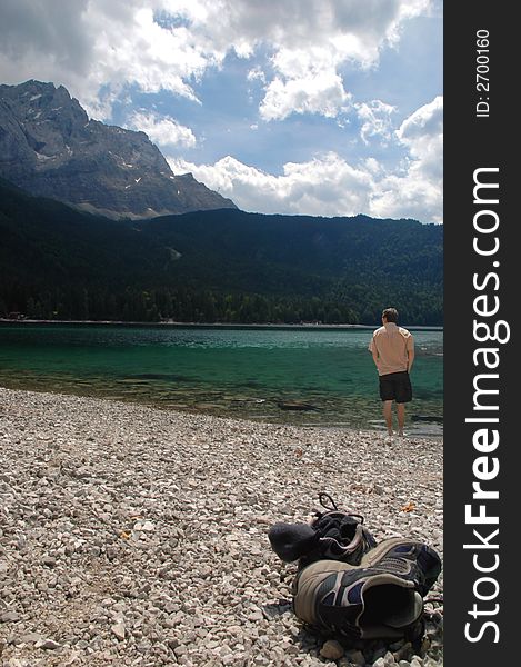 A young man cooling his feet off int he water of a beautiful lake in Bavaria, Germany...his sneakers and socks are laying int he foreground. A young man cooling his feet off int he water of a beautiful lake in Bavaria, Germany...his sneakers and socks are laying int he foreground.