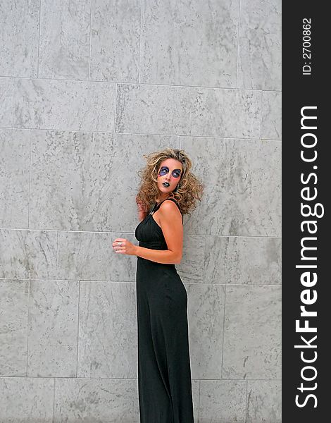 Fashion makeup model in black dress posing against grey wall. Fashion makeup model in black dress posing against grey wall