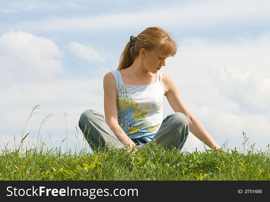 The red girl has a rest at top of a hill, sitting in a grass. The red girl has a rest at top of a hill, sitting in a grass