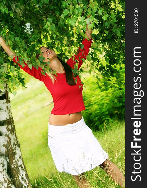 A young beautiful happy woman is laughing against a green tree and a meadow. A young beautiful happy woman is laughing against a green tree and a meadow