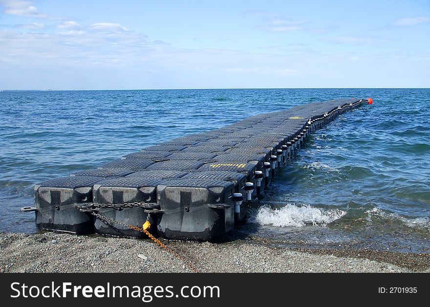 A lone black floating dock in choppy water and the horizon and a blue sky in the background.