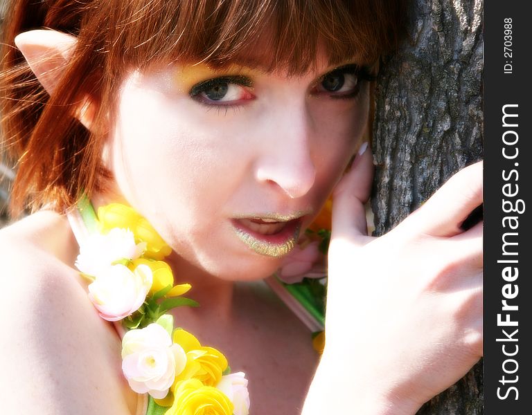 Beautiful pixie woman leaning against tree outdoors.