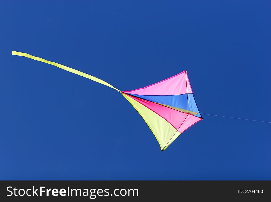 A kite flying against a blue sky in sunlight, bright colors and streaming tail. A kite flying against a blue sky in sunlight, bright colors and streaming tail