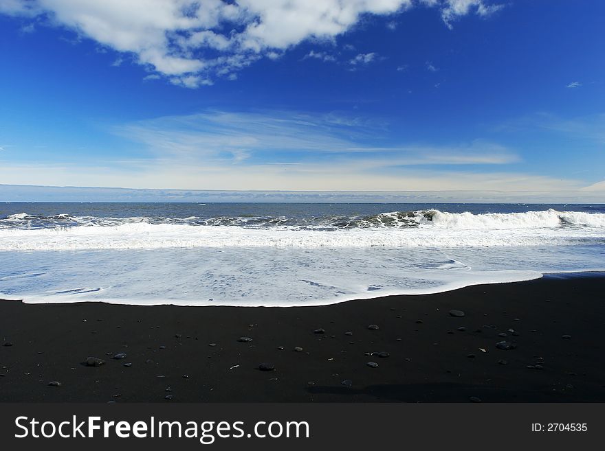 Waves crashing on a sandy black beach , deep blue sky and clouds in background. Waves crashing on a sandy black beach , deep blue sky and clouds in background